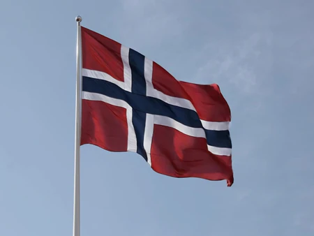 Norsk flagg vaier i toppen av flaggstang mot blå himmel